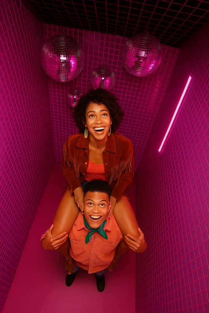 Cabine de photobooth KONEO “Cabine Miroir Disco” : un espace rose vibrant orné de boules à facettes et d’un néon fuchsia, parfait pour des selfies originaux et funs entre amis.