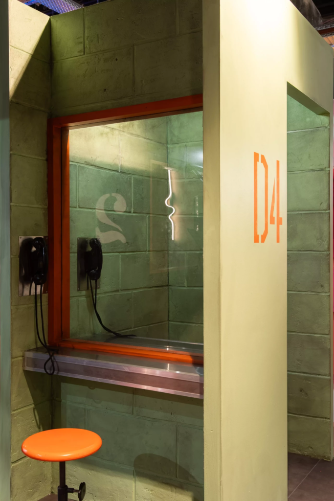 Décor immersif de parloir de prison avec vitre de séparation, téléphones muraux et ambiance carcérale inspirée des films et séries américaines.