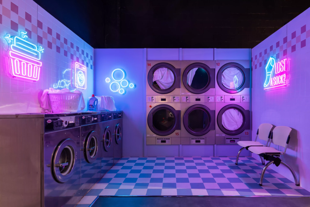 Décor de laverie automatique néon avec machines à laver industrielles, éclairages colorés et ambiance urbaine rétro-futuriste idéale pour shootings photo créatifs.