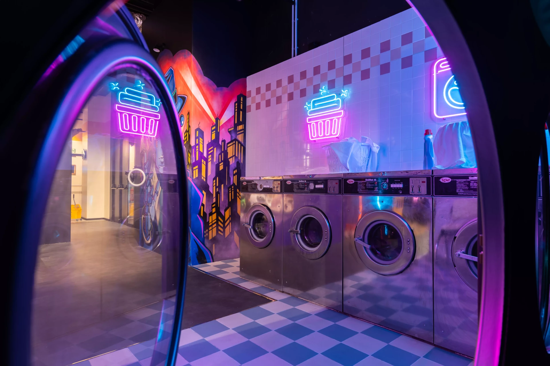 Décor de laverie automatique (vu de l'intérieur d'un sèche linge) néon avec machines à laver industrielles, éclairages colorés et ambiance urbaine rétro-futuriste idéale pour shootings photo créatifs.