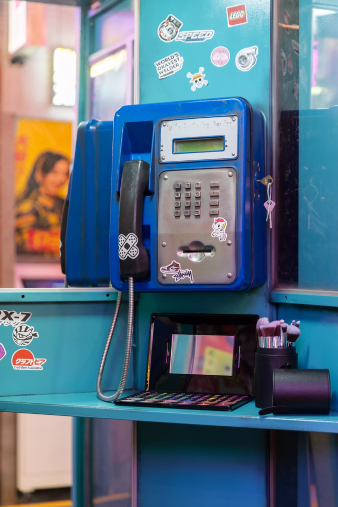 Décor inspiré d’une cabine téléphonique coréenne vintage avec téléphone public bleu, miroir de maquillage, accessoires K-pop et ambiance urbaine néon idéale pour photos immersives à Séoul.