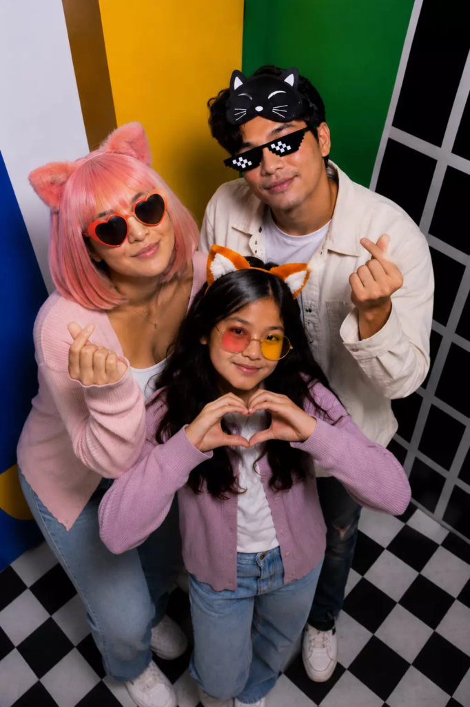 Famille posant dans le photobooth Pop de KONEO Studio à Paris avec accessoires colorés.