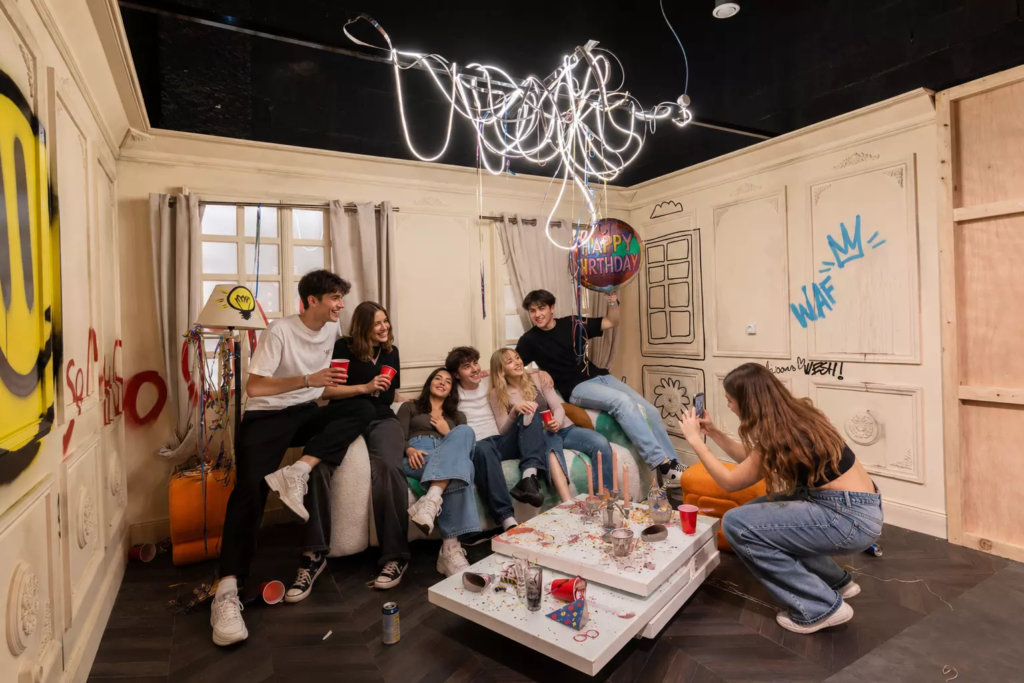 Groupe de 6 jeunes adultes (hommes et femmes) en train de se prendre en photo dans le décor imersif "Hangover" de KONEO Studio, à l'occasion d'un anniversaire